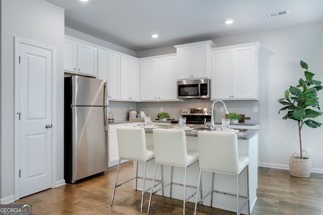 kitchen featuring a center island with sink, stainless steel appliances, hardwood / wood-style floors, and white cabinetry