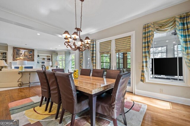 dining room featuring built in shelves, light hardwood / wood-style flooring, ornamental molding, and a chandelier