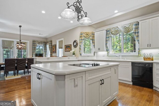 kitchen featuring decorative light fixtures, black appliances, crown molding, white cabinets, and light hardwood / wood-style floors