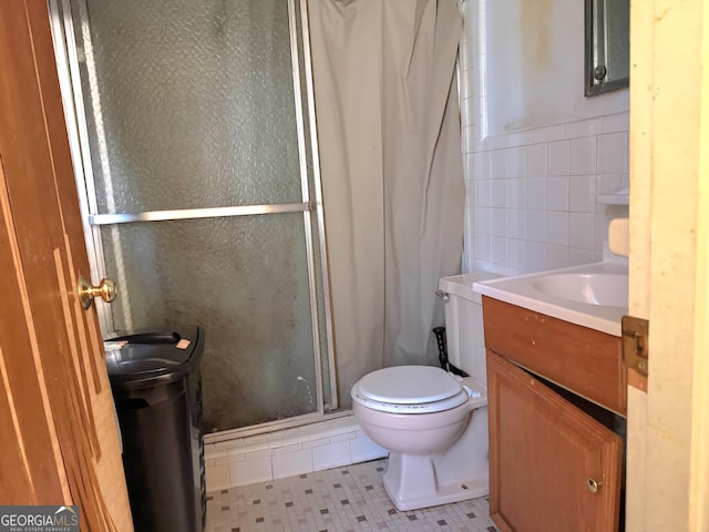 bathroom with vanity, a shower with door, tile patterned flooring, toilet, and tile walls