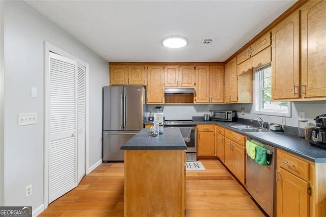 kitchen with stainless steel appliances, dark countertops, a sink, and a center island