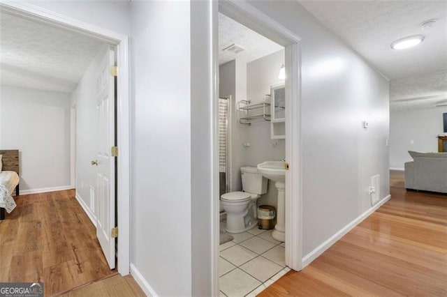 hallway with a textured ceiling, light wood-style flooring, and baseboards