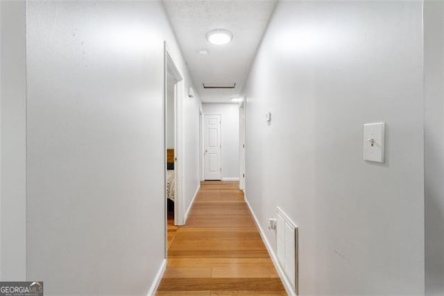 hall featuring attic access, wood finished floors, visible vents, and baseboards