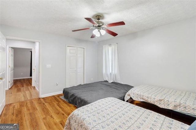 bedroom with a closet, light wood-style floors, a ceiling fan, a textured ceiling, and baseboards