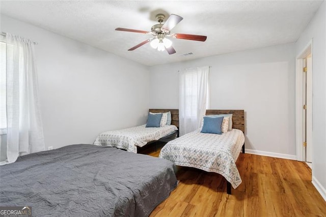 bedroom with a ceiling fan, baseboards, visible vents, and wood finished floors