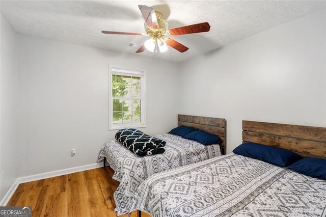 bedroom featuring a ceiling fan, a textured ceiling, baseboards, and wood finished floors