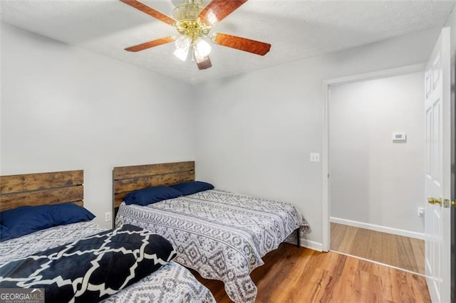 bedroom with a ceiling fan, a textured ceiling, baseboards, and wood finished floors