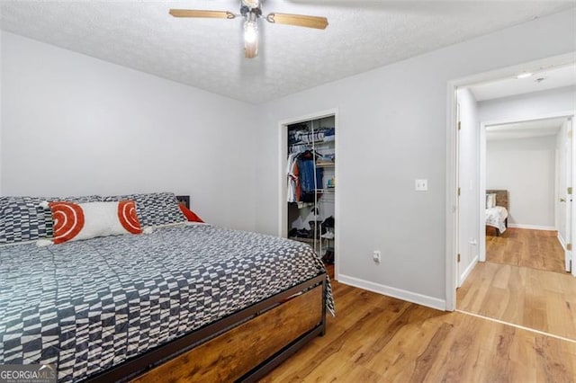 bedroom with a closet, a ceiling fan, a textured ceiling, wood finished floors, and baseboards