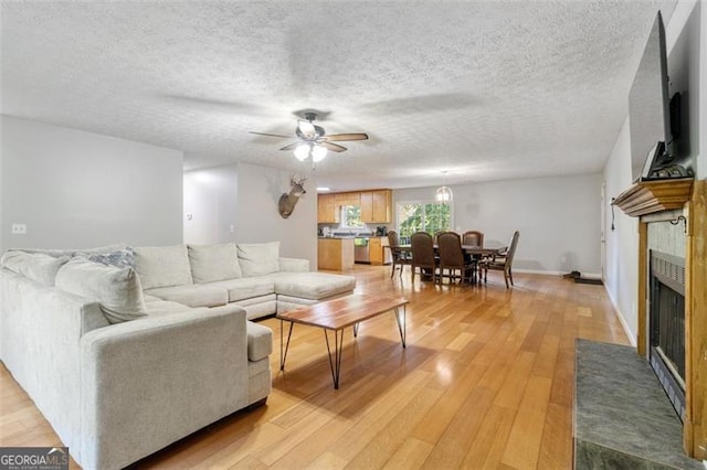 living area featuring a textured ceiling, ceiling fan, baseboards, light wood-style floors, and a tiled fireplace