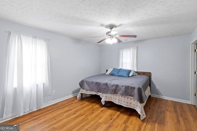 bedroom with ceiling fan, a textured ceiling, baseboards, and wood finished floors