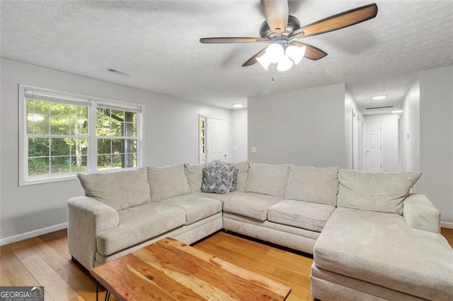 living room featuring a textured ceiling, light wood-type flooring, and baseboards