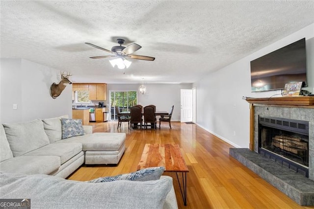 living room with ceiling fan, a textured ceiling, a tiled fireplace, and light wood-style floors