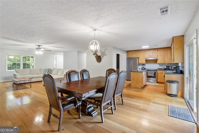 dining room featuring a textured ceiling, ceiling fan with notable chandelier, light wood-type flooring, and visible vents