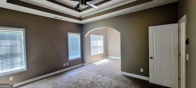 carpeted empty room with ceiling fan, a raised ceiling, and a wealth of natural light