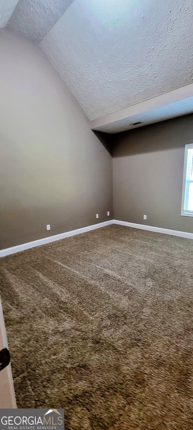 spare room with carpet flooring, a textured ceiling, and vaulted ceiling