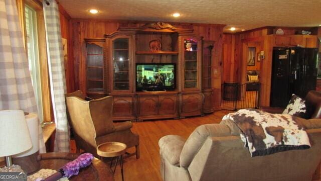 living room with a textured ceiling, light wood-type flooring, and wood walls