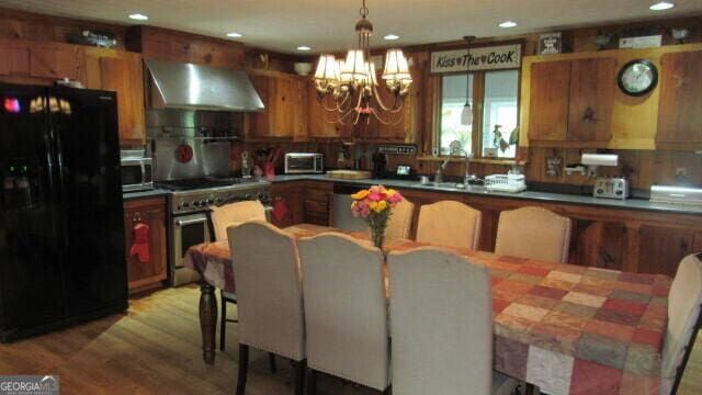 kitchen featuring appliances with stainless steel finishes, wood-type flooring, sink, exhaust hood, and an inviting chandelier