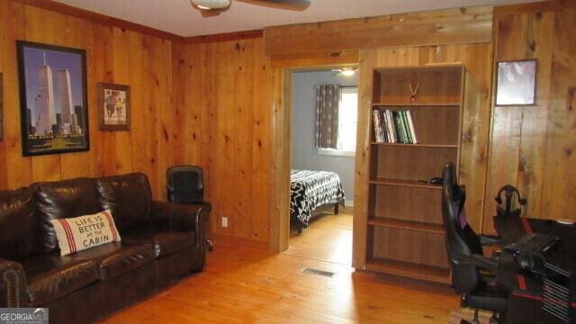 living room with ceiling fan, light wood-type flooring, and wood walls