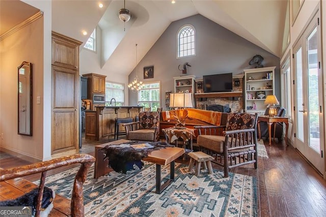 living room featuring dark hardwood / wood-style floors, ceiling fan with notable chandelier, a fireplace, and high vaulted ceiling