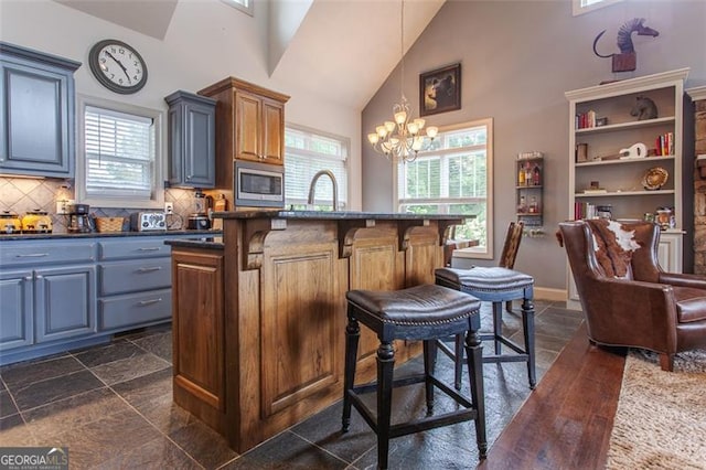 kitchen featuring decorative light fixtures, tasteful backsplash, a chandelier, dark tile patterned floors, and stainless steel microwave