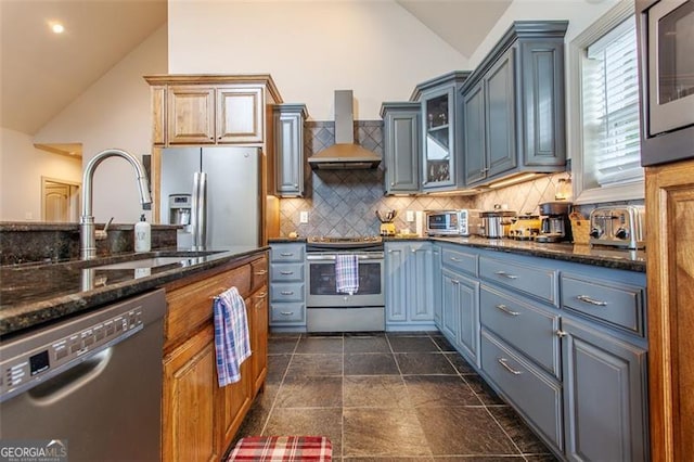 kitchen with dark tile patterned floors, stainless steel appliances, lofted ceiling, and wall chimney range hood