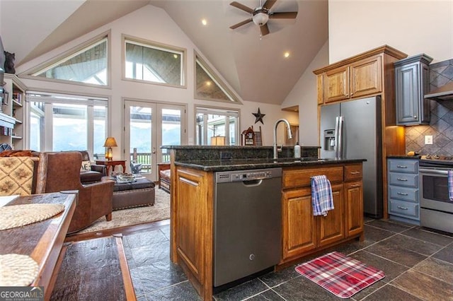 kitchen with backsplash, ceiling fan, an island with sink, stainless steel appliances, and high vaulted ceiling