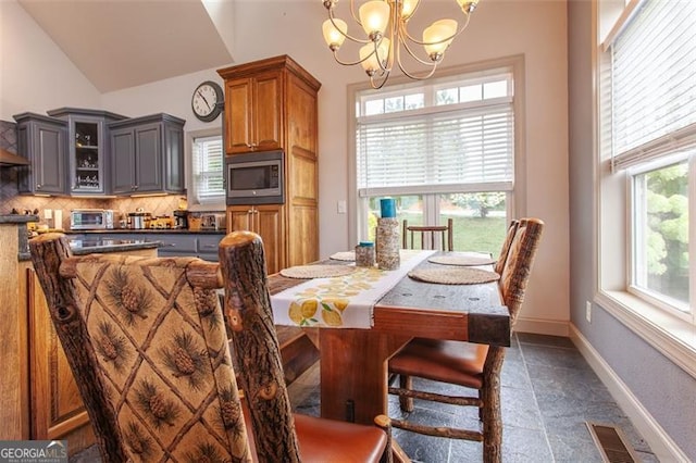 dining space with high vaulted ceiling, dark tile patterned floors, and a notable chandelier