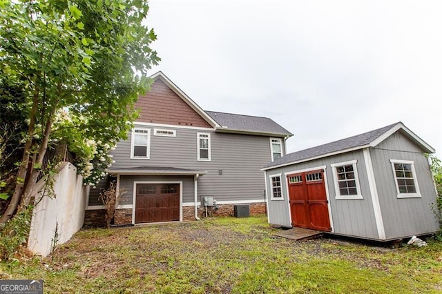 back of house with a garage, central air condition unit, a lawn, and a shed