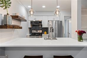 kitchen with a kitchen bar, stainless steel appliances, white cabinets, kitchen peninsula, and hanging light fixtures