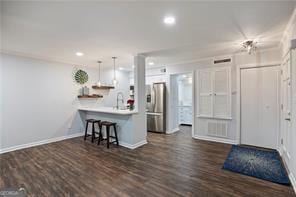 kitchen featuring decorative light fixtures, a kitchen bar, stainless steel fridge, kitchen peninsula, and dark wood-type flooring