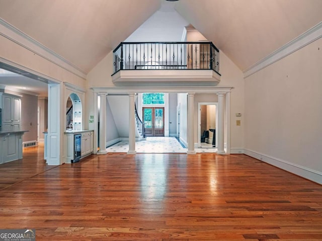 unfurnished living room with beverage cooler, wood-type flooring, decorative columns, and a high ceiling