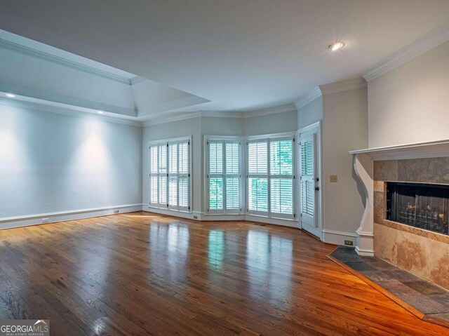 unfurnished living room featuring wood-type flooring, a tiled fireplace, and crown molding