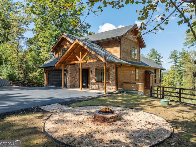 chalet / cabin featuring stone siding, an outdoor fire pit, fence, and aphalt driveway