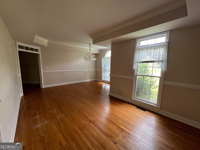 unfurnished room featuring a notable chandelier, ornamental molding, and hardwood / wood-style flooring