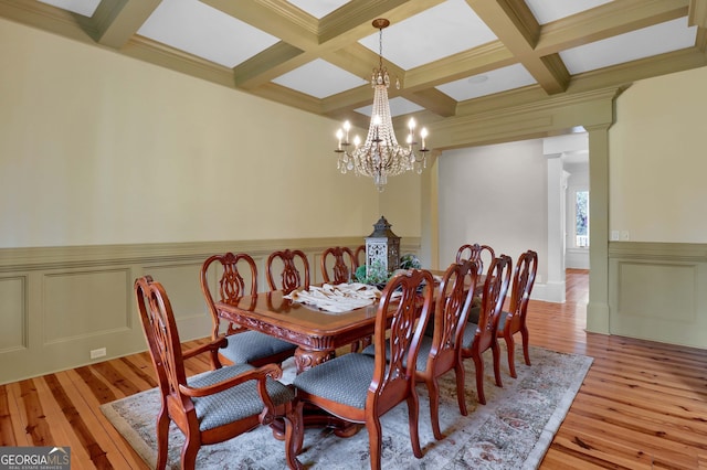 dining area with decorative columns, an inviting chandelier, coffered ceiling, and light wood-type flooring