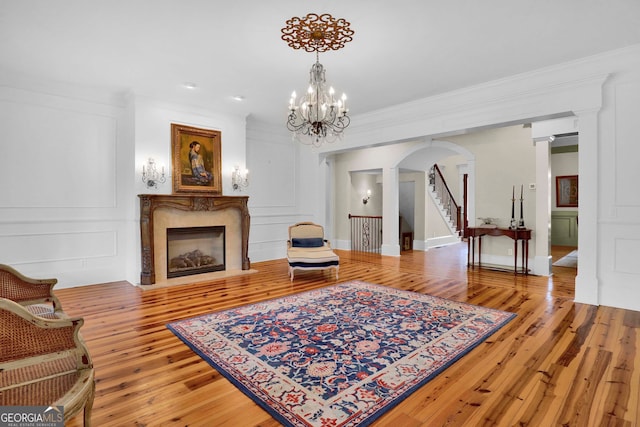 living room featuring a premium fireplace, light wood-type flooring, ornamental molding, an inviting chandelier, and ornate columns