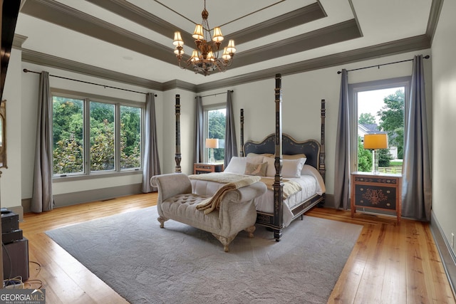 bedroom featuring crown molding, light hardwood / wood-style flooring, a raised ceiling, and a notable chandelier