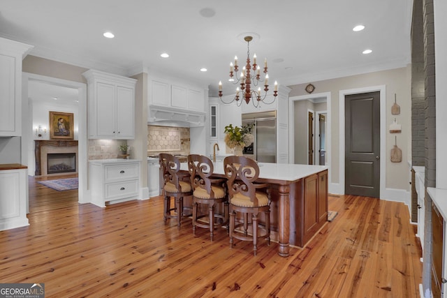 kitchen with light hardwood / wood-style floors, stainless steel built in fridge, white cabinets, and an island with sink