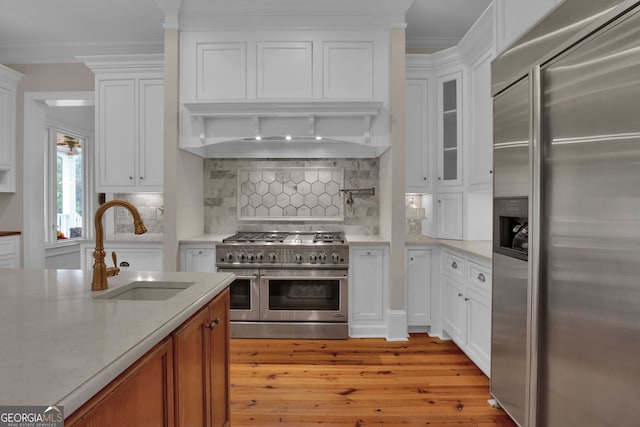 kitchen with decorative backsplash, high quality appliances, white cabinets, and light hardwood / wood-style floors