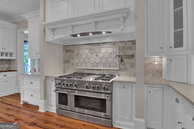 kitchen with range with two ovens, tasteful backsplash, white cabinets, light wood-type flooring, and ornamental molding