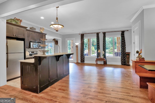 kitchen with light hardwood / wood-style flooring, a kitchen island with sink, stainless steel appliances, decorative backsplash, and decorative light fixtures