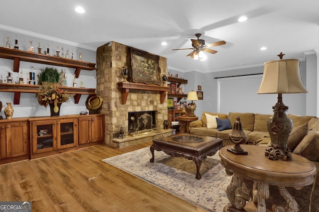 living room with crown molding, a stone fireplace, hardwood / wood-style floors, and ceiling fan