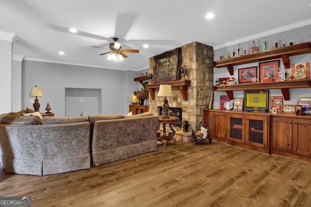 living room featuring a fireplace, wood-type flooring, crown molding, and ceiling fan