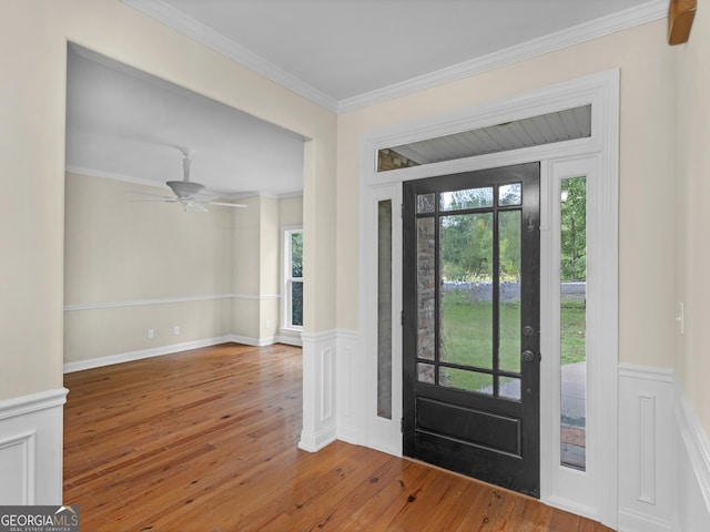 foyer entrance featuring wood-type flooring, crown molding, a wainscoted wall, and ceiling fan