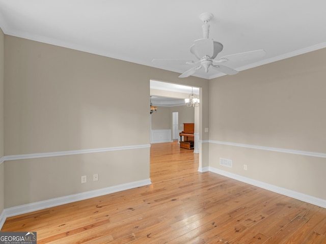 spare room featuring ceiling fan with notable chandelier, baseboards, wood finished floors, visible vents, and ornamental molding