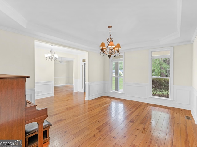 interior space with an inviting chandelier, ornamental molding, a tray ceiling, and light hardwood / wood-style flooring