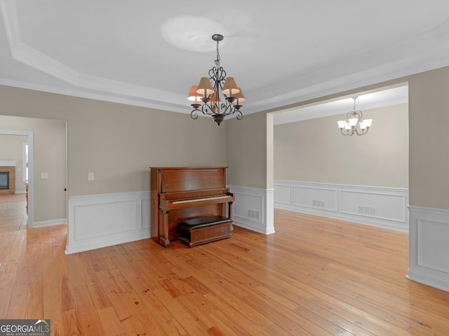 unfurnished dining area with an inviting chandelier, ornamental molding, a fireplace, and light hardwood / wood-style floors