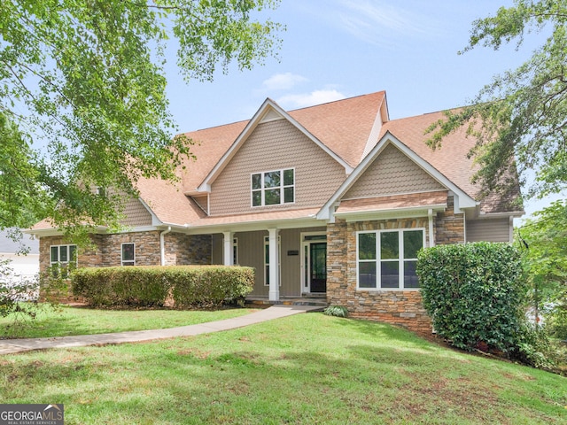 craftsman house with covered porch, roof with shingles, stone siding, and a front lawn