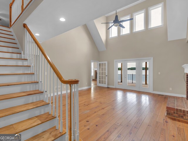 foyer featuring a brick fireplace, a towering ceiling, ceiling fan, and light wood-type flooring