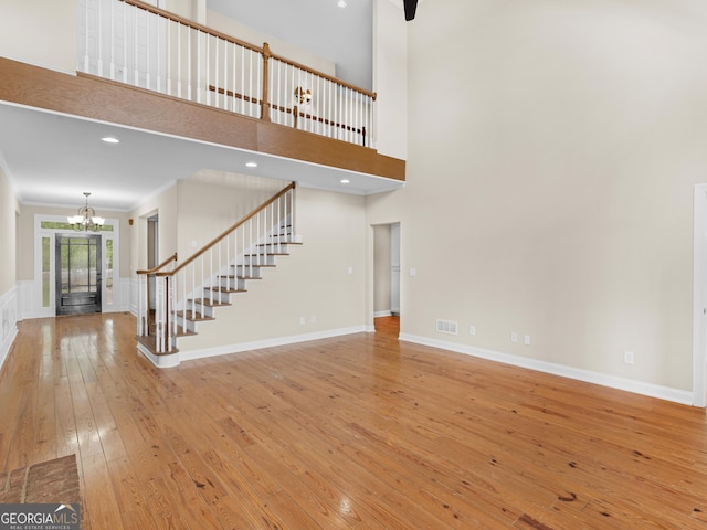 unfurnished living room featuring an inviting chandelier, visible vents, stairs, hardwood / wood-style floors, and a high ceiling